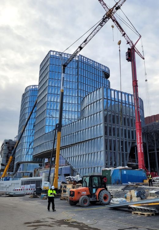 Chantier de construction d'un bâtiment moderne avec façade en bardage aluminium et vitrage, illustrant le montage de panneaux de verre à l'aide de grues Chantier de construction d'un bâtiment moderne avec façade en bardage aluminium et vitrage, illustrant le montage de panneaux de verre à l'aide de grues